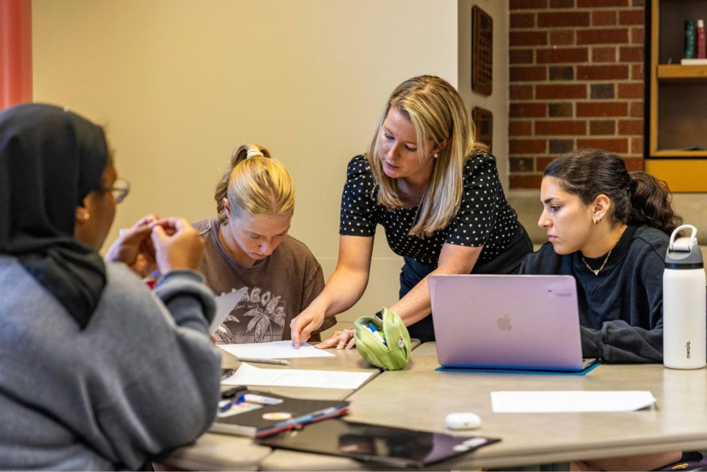 A Human Development and Family Science faculty helps college students at a table during a class session.