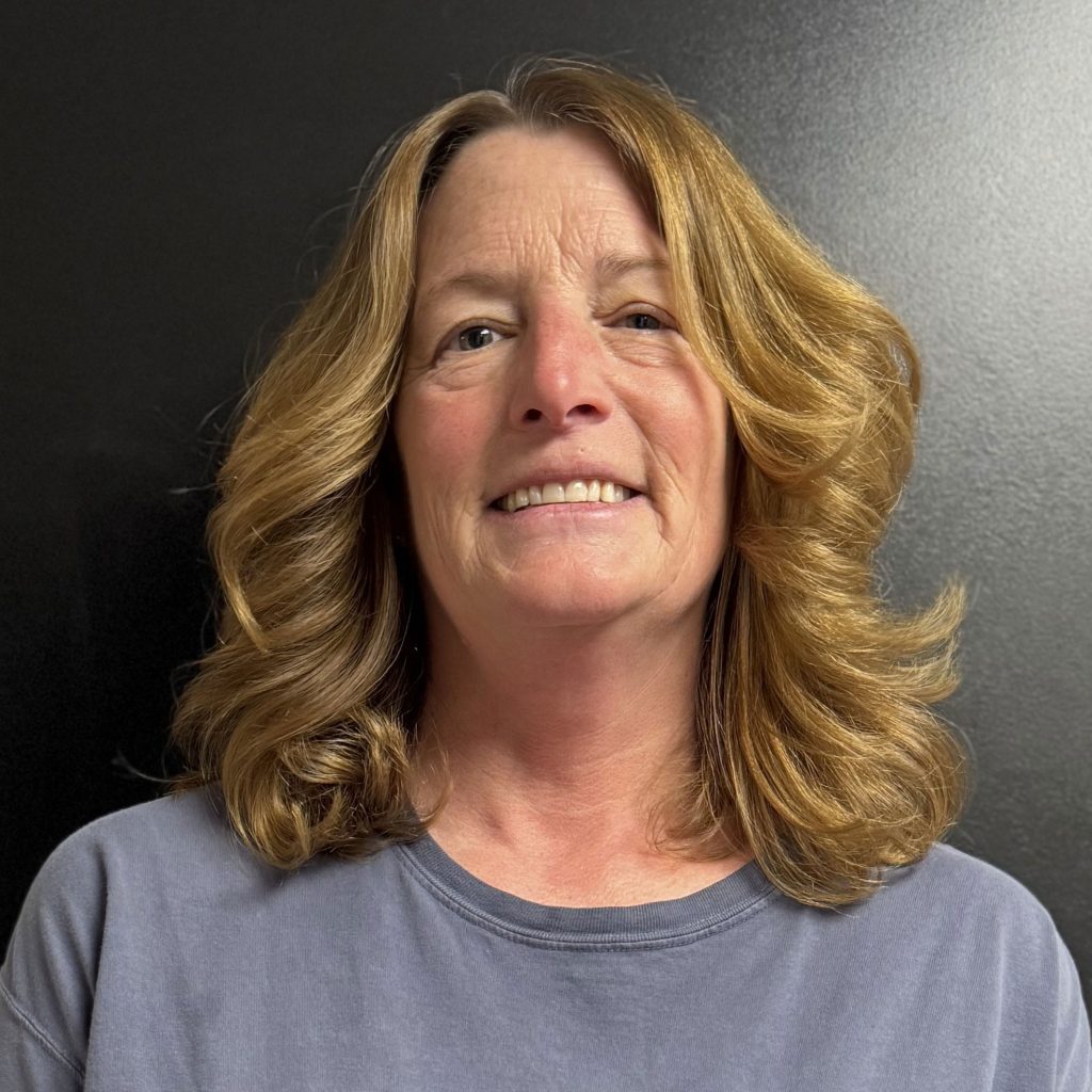 A woman with blonde hair wearing a grey shirt.