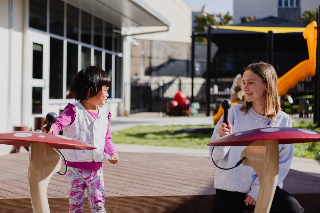 A young child plays on the drums with an early childhood professional in the outdoor classroom at the Child Development Lab.