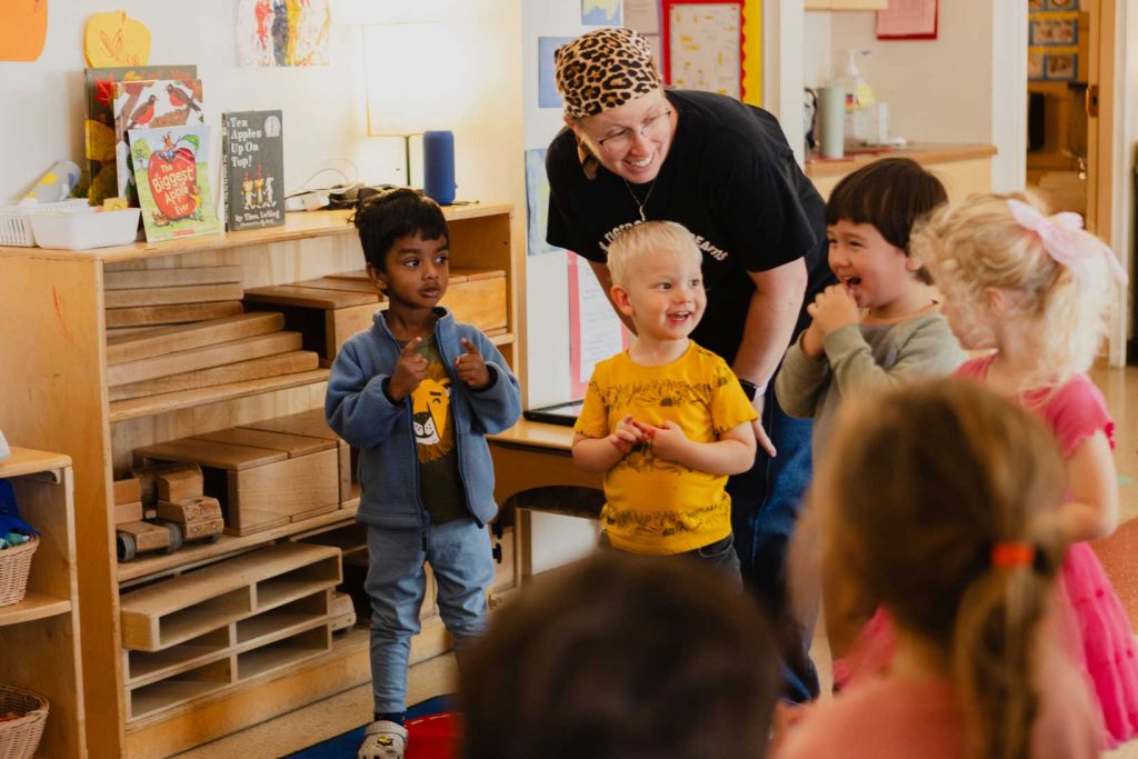 An early childhood teacher smiles while working with preschool aged children in a classroom.