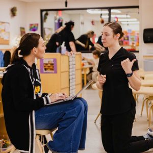 Two early childhood professionals talk in purple door at the Child Development Lab.
