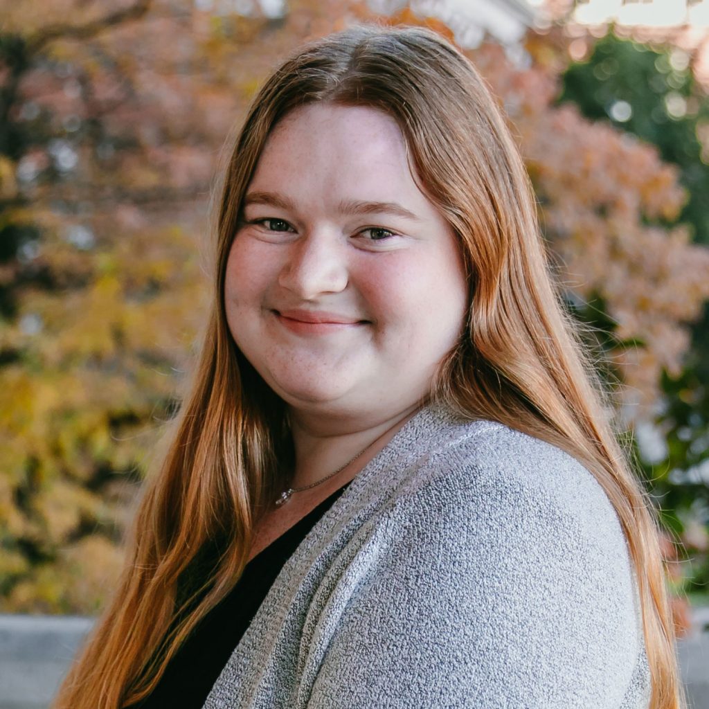 A woman with long red hair wearing a grey sweater.