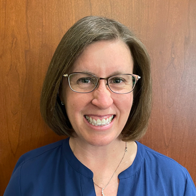 A woman with glasses and short brown hair wearing a blue shirt.