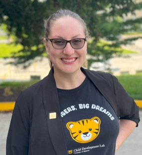 A picture of a woman with glasses and dark hair pulled back, wearing a black CDL shirt with a tiger on it.