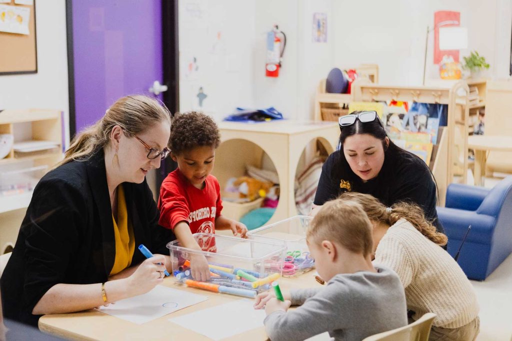 Two early childhood professionals work with preschool aged children at a table in Purple Door at the Child Development Lab.