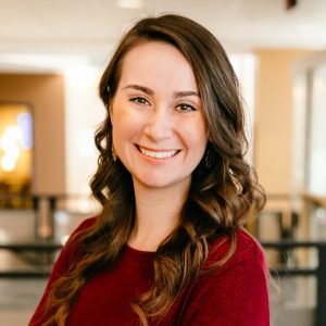 A woman with long brown hair wearing a red sweater.