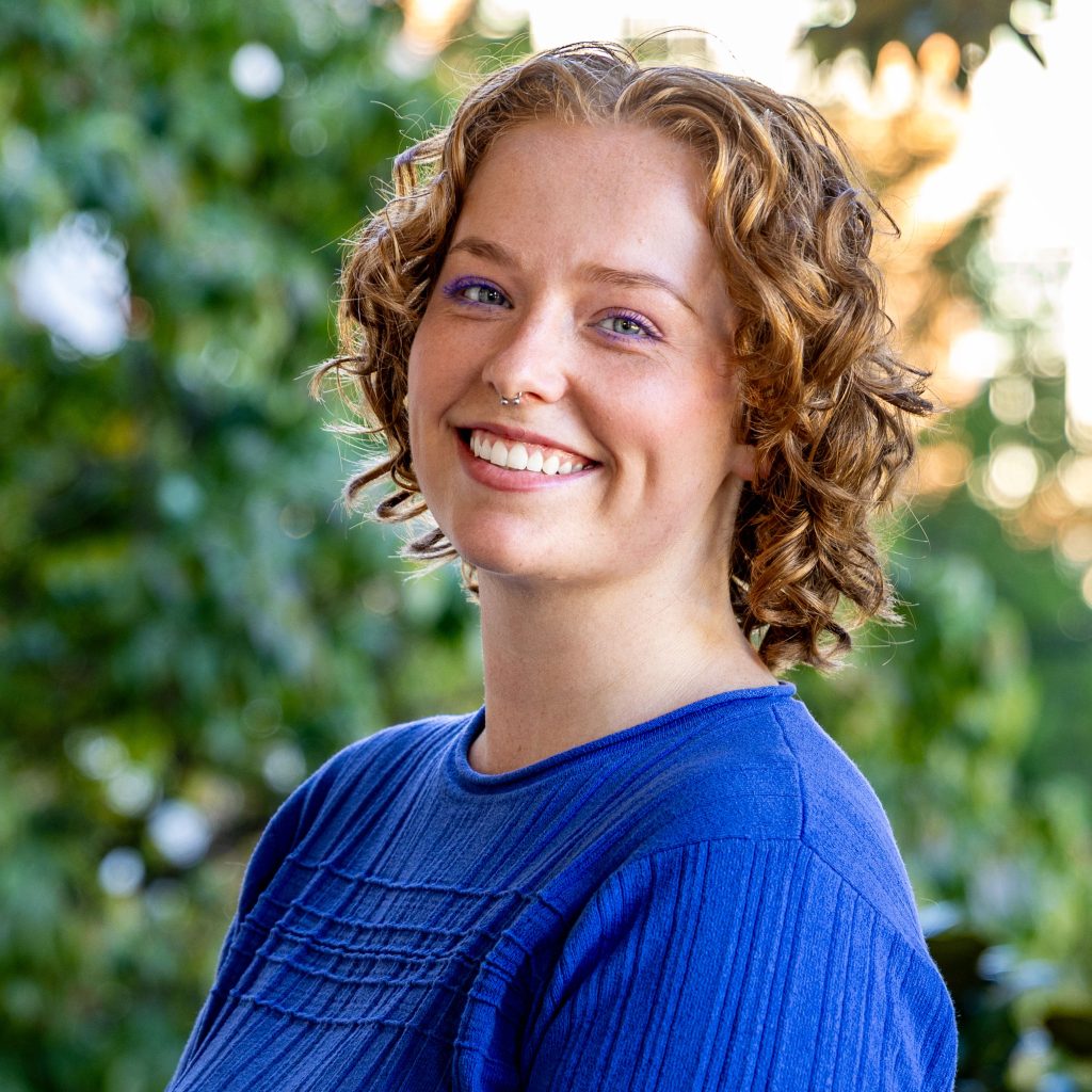 A woman with short, curly blond hair wearing a blue sweater.