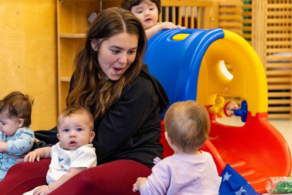 An early childhood teacher sits on the floor with babies in the Blu Door classroom at the Child Development Lab.
