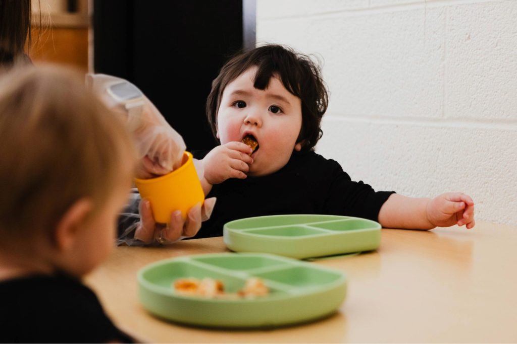 Two babies eat family style at a table in Blue Door at the Child Development Lab.