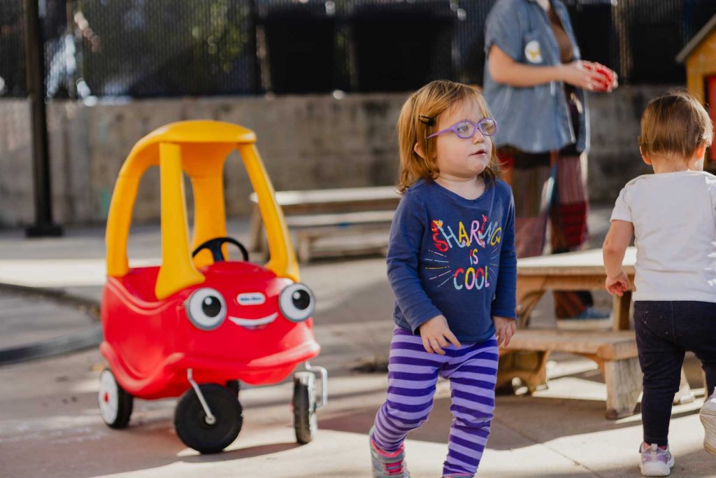 A young girl wearing purple glasses plays outside in the outdoor classroom at the Child Development Lab.