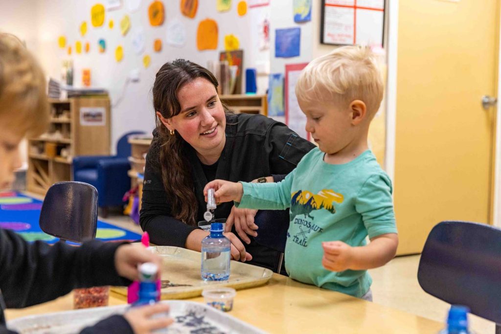An early childhood teacher helps a child with an activity in green door at the Child Development Center.
