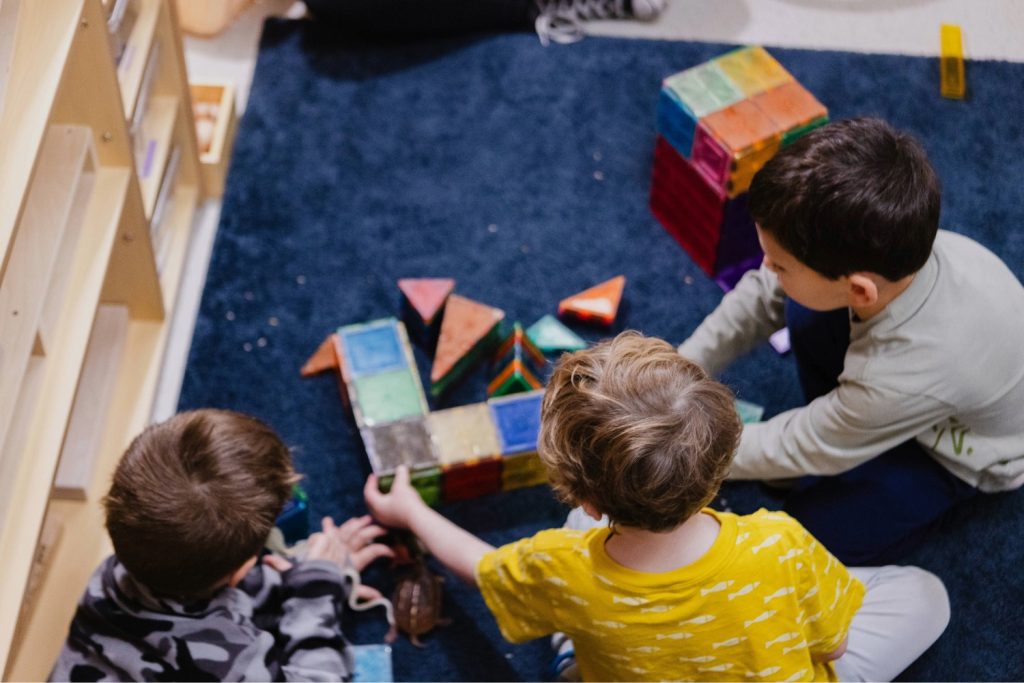 Three young boys play with building blocks on a blue carpet in a classroom at the Child Development Lab.