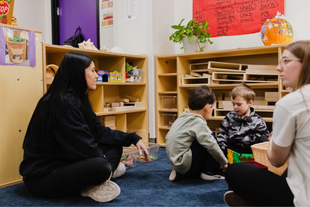 Two early childhood professionals sit on the floor with preschool aged children as they play in purple door at the Child Development Lab.