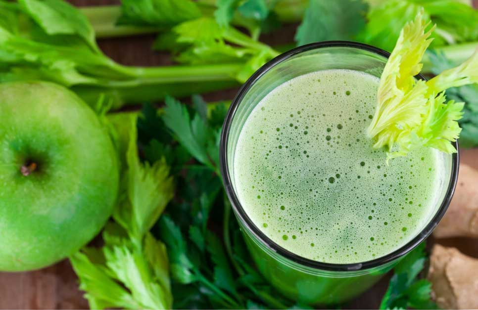 Green apple and celery next to a glass of green juice.